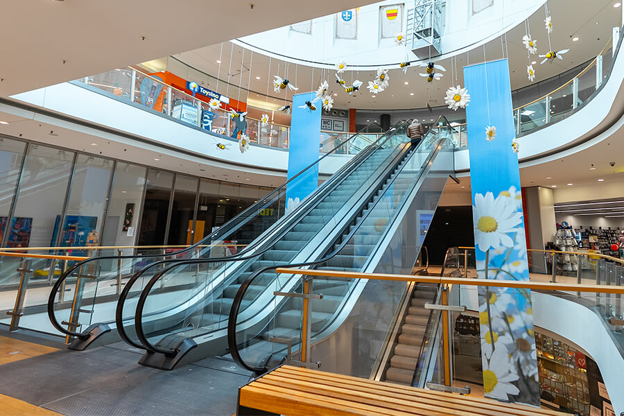 Zwei nebeneinander verlaufende Rolltreppen mit hängenden Dekorationen und Sitzbank im Vordergrund