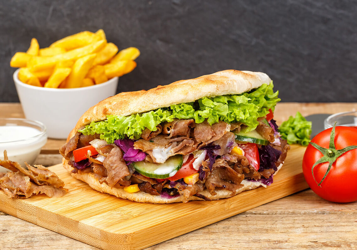 Saftiger Döner auf einem Holzbrett angerichtet mit einer Schale Pommes daneben