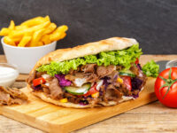 Saftiger Döner auf einem Holzbrett angerichtet mit einer Schale Pommes daneben